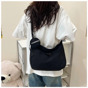 Détail d'un sac bandoulière noir avec large bandoulière et pendentif porte-monnaie rond