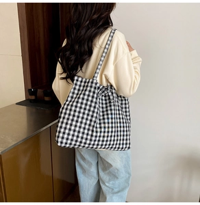 Dettaglio della borsa tote a scacchi bianchi e neri con un fiocco decorativo sulla tracolla
