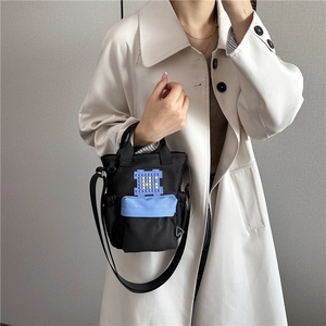 Black nylon crossbody bag with blue front pocket and pixelated purple H patch