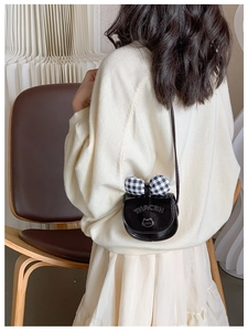 Girl wearing a black mini crossbody bag with a checkered bow and cat print detail