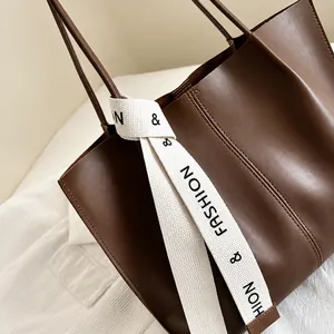Close-up of brown leather tote bag showing fine stitching and fashion decorative ribbon