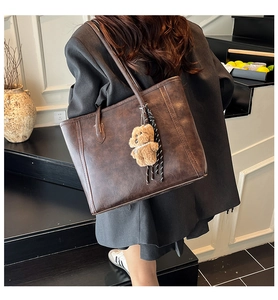 Detail of dark brown leather tote bag with cute bear charm and woven tassel detail
