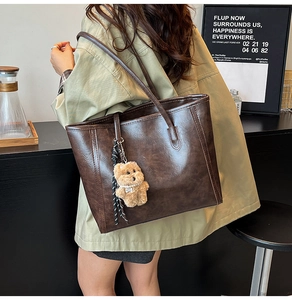 Detail of vintage textured leather tote bag with cute plush bear charm on model's shoulder
