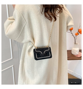 Detalle de bolso bandolera de ante negro con costuras en V blancas y cadena dorada