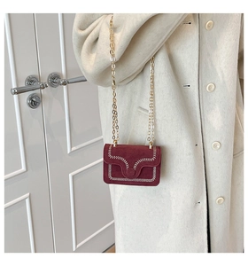 Detalle de mini bolso de ante burdeos con costuras blancas y cadena dorada