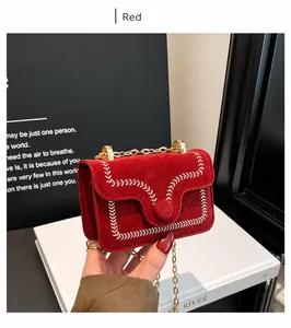 Detail van rode suède crossbodytas met wit stikselpatroon en gouden kettingriem