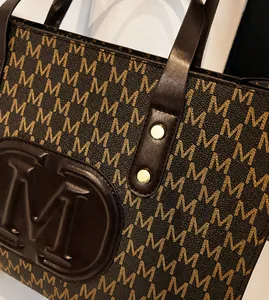 Detailaufnahme der braunen Ledertasche mit M-Monogramm-Drucken und goldenen Metallbeschlägen