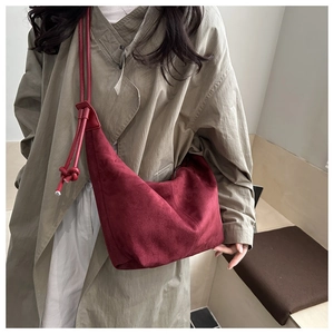 Detailed view of a burgundy suede hobo bag with an elegant knot strap on a beige trench coat