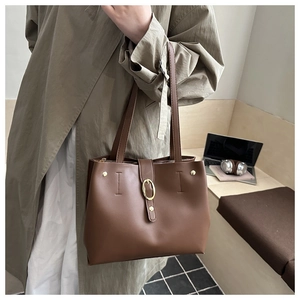 Close-up of brown leather tote bag with elegant gold buckle and office laptop
