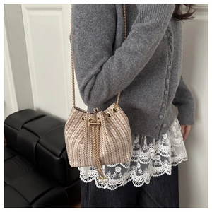 Détail du sac seau tissé beige avec cordon, chaîne dorée et détails de perles