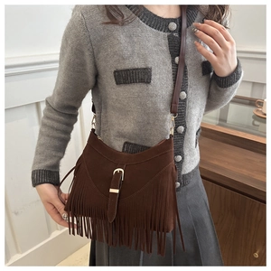 Detail of a brown suede crossbody bag featuring long fringes and a vintage metal buckle