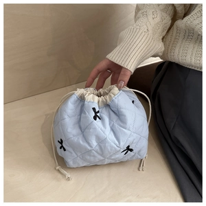 Gros plan du sac matelassé bleu clair avec broderie nœud noir et cordon de serrage