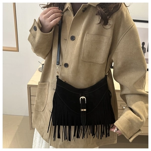 Detail of a black suede tassel crossbody bag with gold buckle on a khaki jacket