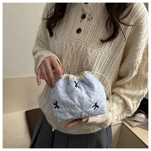 Detail of light blue quilted drawstring bucket bag featuring black bow embroidery patterns