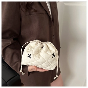 Detail of off-white quilted bucket bag featuring drawstring closure and floral embroidery