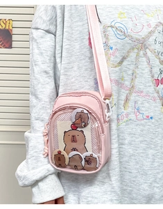 Detail of pink ita bag with clear PVC window showing capybara pins and charms