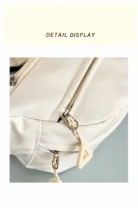 Detail view of smooth dual metal zippers and nylon fabric pulls on the cream chest bag