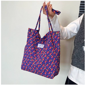 Detail van een paarse gewatteerde tote bag met bloemenprint en wit merklabel in de hand