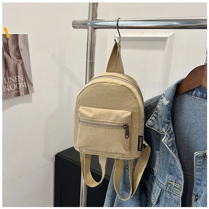 Dettaglio di un mini zaino in nylon beige appeso a un supporto davanti a una giacca di jeans