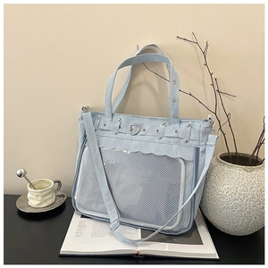 Detail of light blue itabag showing heart-shaped buckle and mesh clear pocket on canvas