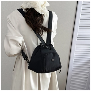 Vista trasera de modelo con mochila triangular de nailon negro sobre gabardina beige