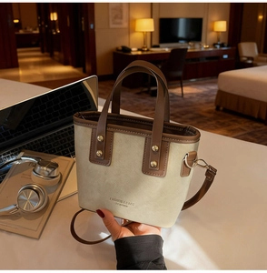 Vue détaillée du sac seau beige avec poignées en cuir marron et finitions métalliques