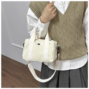 Detail view of a cream canvas crossbody bag with adjustable straps and round logo