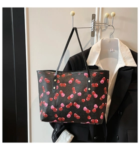 Detalle de un bolso tote negro grande con estampado de cerezas colgado en una pared blanca