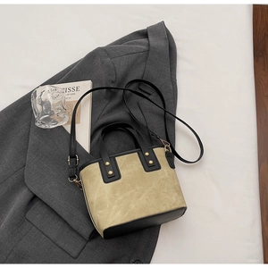 Détail du sac beige en daim et cuir noir avec rivets dorés posé sur un blazer gris