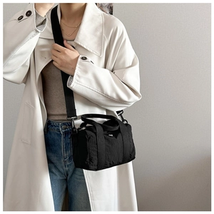 Minimalist black nylon crossbody bag styled with a trench coat and adjustable shoulder strap