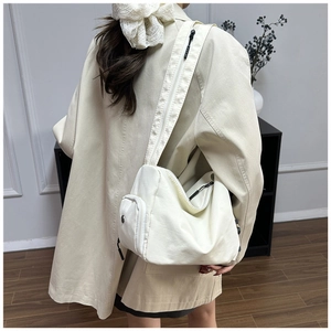 Detalle de bolso bandolera de lona beige con gran capacidad y bolsillo frontal con cremallera
