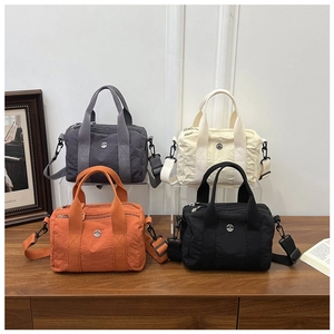 Front view of small canvas crossbody bags in gray, white, orange, and black on a wooden desk