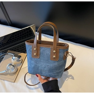Détail du sac seau en denim bleu avec lanières en cuir marron et rivets dorés