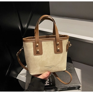 Détail du sac cabas en toile montrant les rivets dorés et les coutures en cuir brun