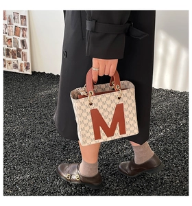 Detail view of cream tote bag with monogram texture and brown leather M letter applique
