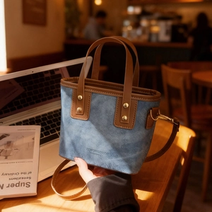 Sac fourre-tout en denim bleu avec bordure en cuir marron et rivets dorés sur table