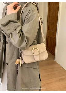 Detail der beigen Wildledertasche mit goldener Rundschnalle und Baseball-Anhänger-Zubehör