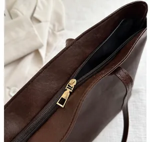 Detail view of smooth golden metal zipper on dark brown vintage faux leather tote bag