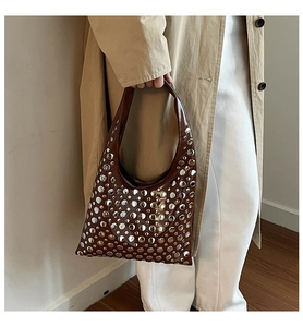 Détails des rivets argentés sur un sac hobo marron porté avec un trench décontracté
