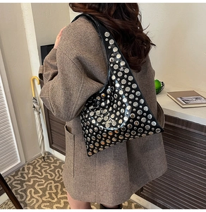 Detail of black glossy shoulder bag with silver rivet studs on a model in brown plaid