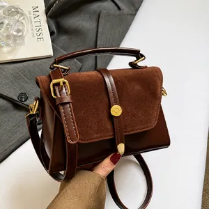 Detail of dark brown leather crossbody bag with suede stitching and gold metal buckle