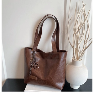 Detail of brown faux leather tote bag with round charm and fashion label on table