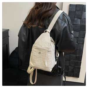 Detail of a creamy white nylon crossbody bag featuring wrinkled fabric and a round metal logo