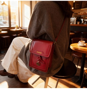Detail of red leather mini bag with yellow 'Fashion' text and metal pendant in soft light