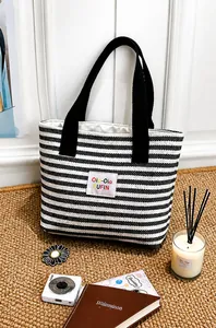 Nahaufnahme der schwarz-weiß gestreiften Canvas-Einkaufstasche mit Logo-Patch auf Teppich