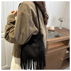 Détail d'un sac seau noir en daim à franges montrant le style bohème et la bandoulière