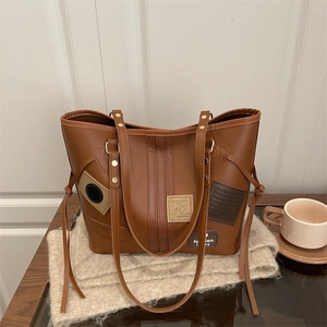 Retro brown leather tote bag with decorative patches and long fringe on neutral background