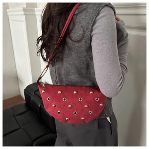 Side view of red suede crescent bag with gold rivets and metallic eyelet details