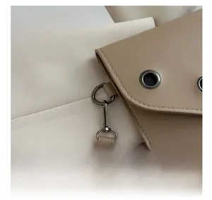 Detailed close-up of dark metallic ring hardware and stitching on beige leather handbag