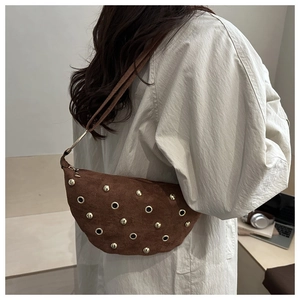 Detalle de bolso hobo de ante marrón con remaches y ojales dorados en una modelo